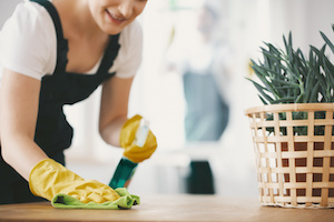 Close-up on smiling housewife with yellow gloves cleaning table with cloth